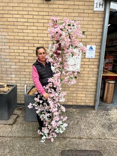 a woman standing next to a tree with pink flowers