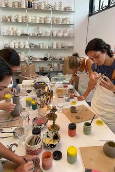 three women working on pottery at a table with cups and saucers in front of them