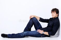 a young man sitting on the floor with his legs crossed, wearing jeans and a black shirt