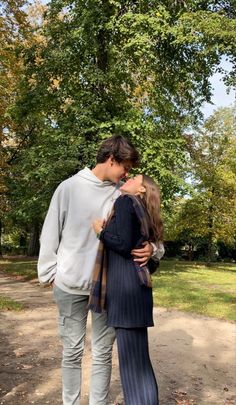 a man and woman standing next to each other in front of trees with leaves on the ground