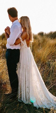 a man and woman standing next to each other in tall grass with their arms around each other