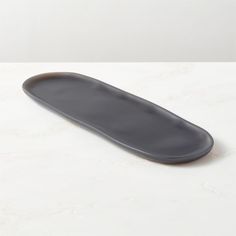 a gray tray sitting on top of a white counter next to a black plate with an oval shape