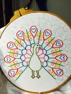 a white embroidered peacock with hearts on it's tail is shown in front of a yellow hoop