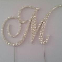 a cake topper with pearls on it and the letter m spelled out in large letters