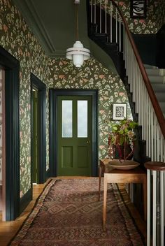 a green door in a hallway with floral wallpaper on the walls and carpeted floor