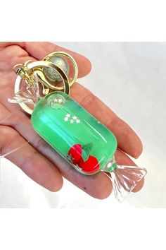 a person is holding a green bottle with a red heart on it and a gold keychain