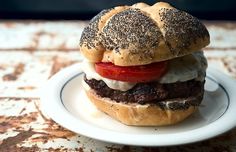 a hamburger with meat, cheese and tomatoes on a bun sitting on a white plate