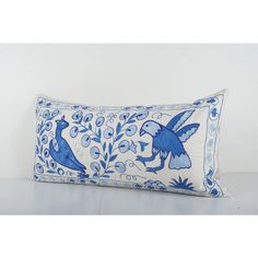 a blue and white decorative pillow with two birds on the front, sitting on a table