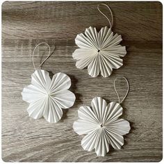 three white paper flowers hanging from strings on a wooden table with string attached to them