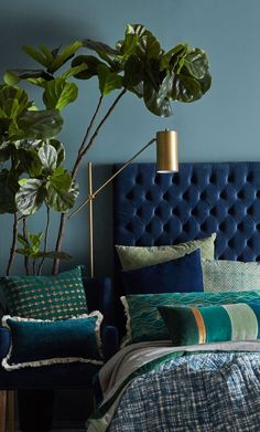 a bedroom with blue walls and green plants on the headboard, bed linens and pillows