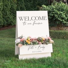 a welcome sign in the grass with flowers on it