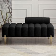 a black couch sitting on top of a wooden floor next to a white wall with gold legs