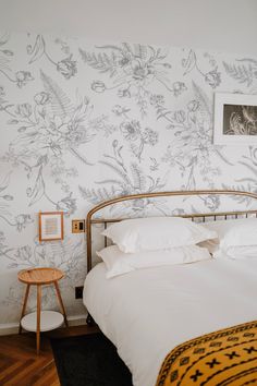 a white bed sitting next to a wall with flowers on it