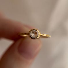 a close up of a person's hand holding a gold ring with a brown diamond