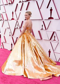 a woman in an orange and gold gown standing on the red carpet at oscars