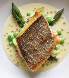 a white plate topped with fish and asparagus on top of a sauce covered dish