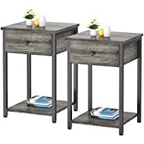 two grey wood side tables with one drawer and the other shelf holding books, candles and flowers