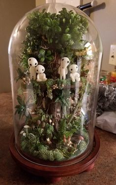 a glass dome filled with plants and small stuffed animals on top of a wooden base