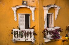 two windows with white shutters and flower boxes on the side of a yellow building