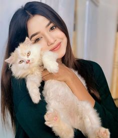 a woman holding a white cat in her arms and looking at the camera with an intense smile on her face