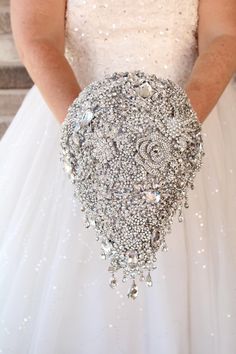 a woman in a white wedding dress holding a silver brooch on her left hand