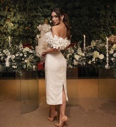 a woman wearing a white dress standing in front of flowers and candles with her back to the camera