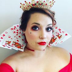 a woman in a red dress wearing a crown and holding playing cards on her head