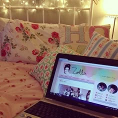 an open laptop computer sitting on top of a bed next to pillows and blankets with lights