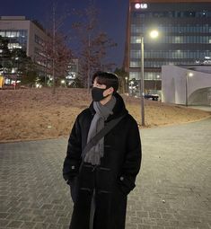 a man wearing a face mask standing in front of a building at night with his hands on his hips