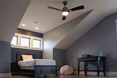 an attic bedroom with hardwood floors and gray walls, along with a ceiling fan that lights up the room