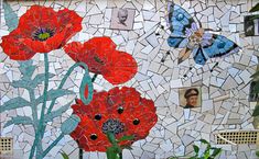 some red flowers are in front of a mosaic wall with pictures and butterflies on it