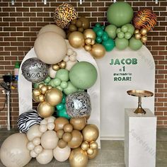 balloon arch with gold, silver and green balloons in front of a brick wall that reads jacob