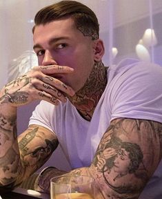 a tattooed man sitting at a table with his hands on his face and looking off to the side