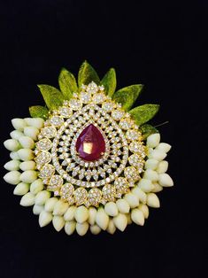 the brooch is adorned with white flowers and green leaves, which are accented with a large red stone