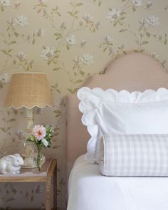 a white bed sitting next to a night stand with flowers on it and a lamp