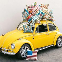 a yellow vw bug with pillows on the roof is parked in front of a white wall