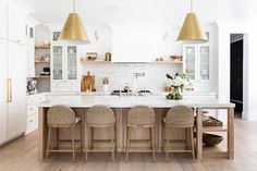 a kitchen with white cabinets and gold pendant lights hanging from the ceiling over the island