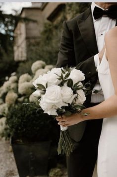 a bride and groom standing next to each other in front of some bushes with white flowers