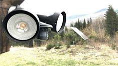 an image of a camera that is on top of a pole in the grass with trees behind it