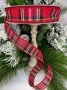 a red plaid ribbon on top of a christmas tree with pine cones and evergreen branches