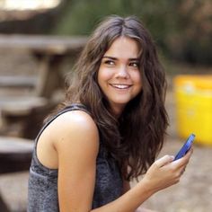 a woman sitting on the ground holding a cell phone in her hand and smiling at the camera