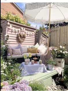 an outdoor patio with flowers and plants on the table, next to a wooden fence