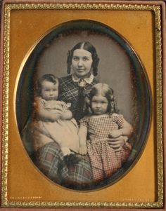 an old - fashioned photo of a woman with two children in her lap, and the child is wearing a plaid dress