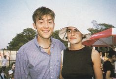 a man and woman standing next to each other in front of an outdoor area with umbrellas