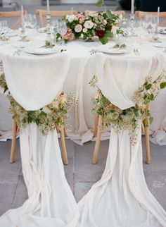 the table is set with white linens and floral centerpieces, along with wooden chairs