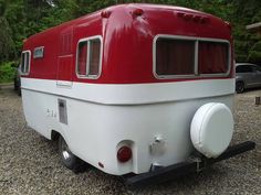 an old red and white trailer parked on gravel