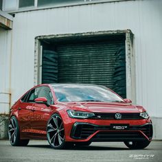 a red volkswagen car parked in front of a building with an open garage door behind it