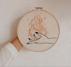 a person holding up a hand embroidered artwork with fire and stars in the sky on it