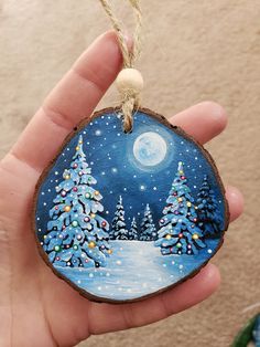 a hand holding a painted ornament with trees on it and the moon in the sky