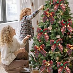 two women decorating a christmas tree with red, green and gold bow decorations on it